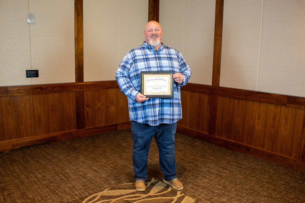 Man in blue plaid shirt holding a certificate