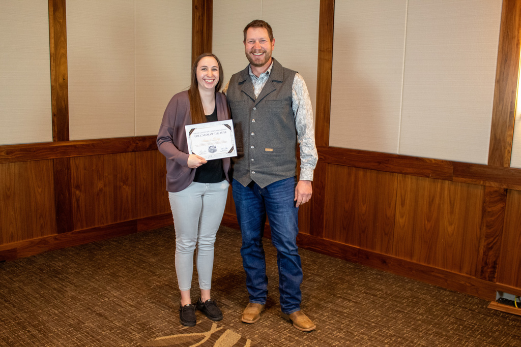 Man in jeans and a vest standing next to woman in sweater and slacks holding a certificate