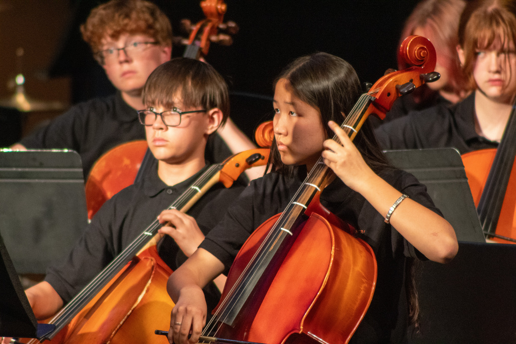 Two students with black hair looking up as they play a chello