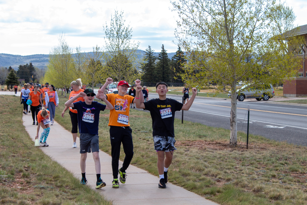 Three boys raising both hands in celebration as they walk sidewalk