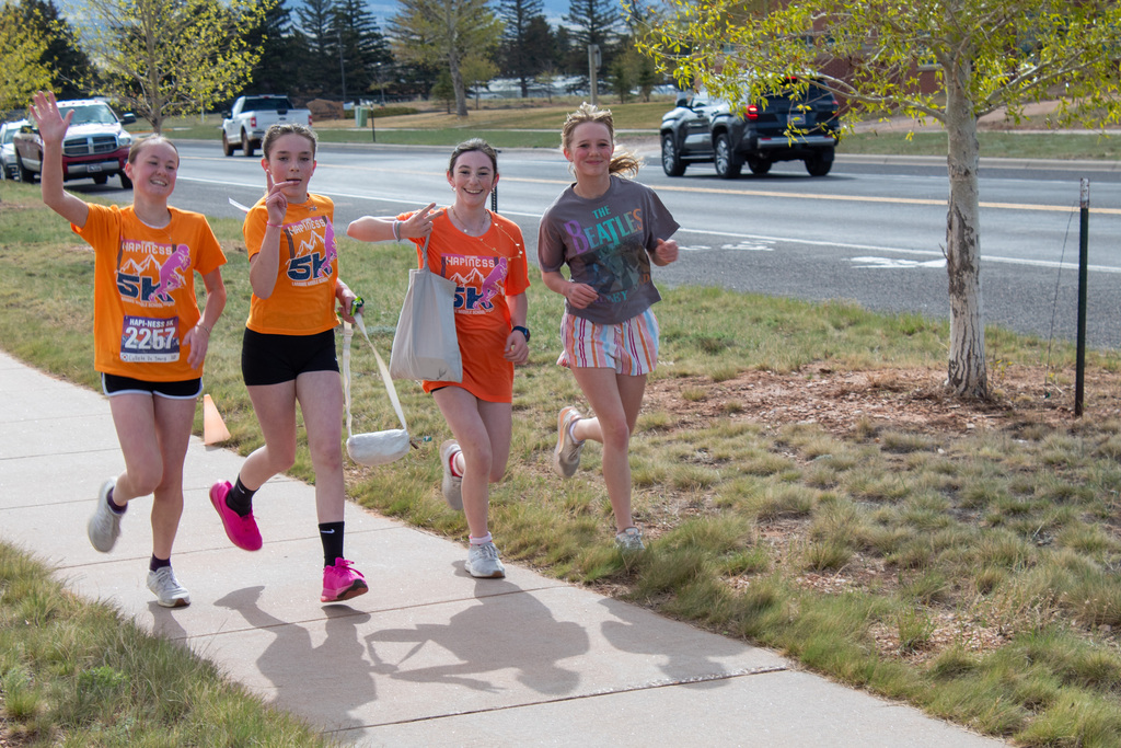 Four girls in orange shirts running and waving while carrying bags