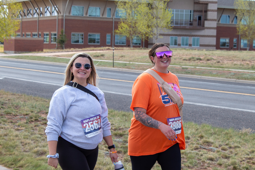Woman with blonde hair and gray shirt walking with woman in sunglasses and orange shirt