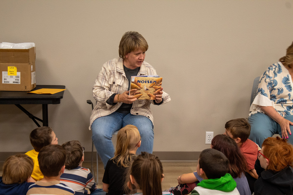 Female in jeans and a flannel reading to a group of students