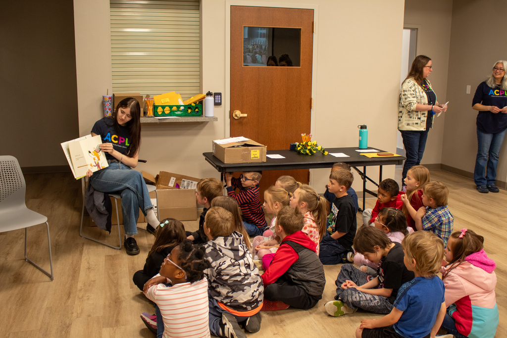 Female in jeans and a black t-shirt reading to a group of students