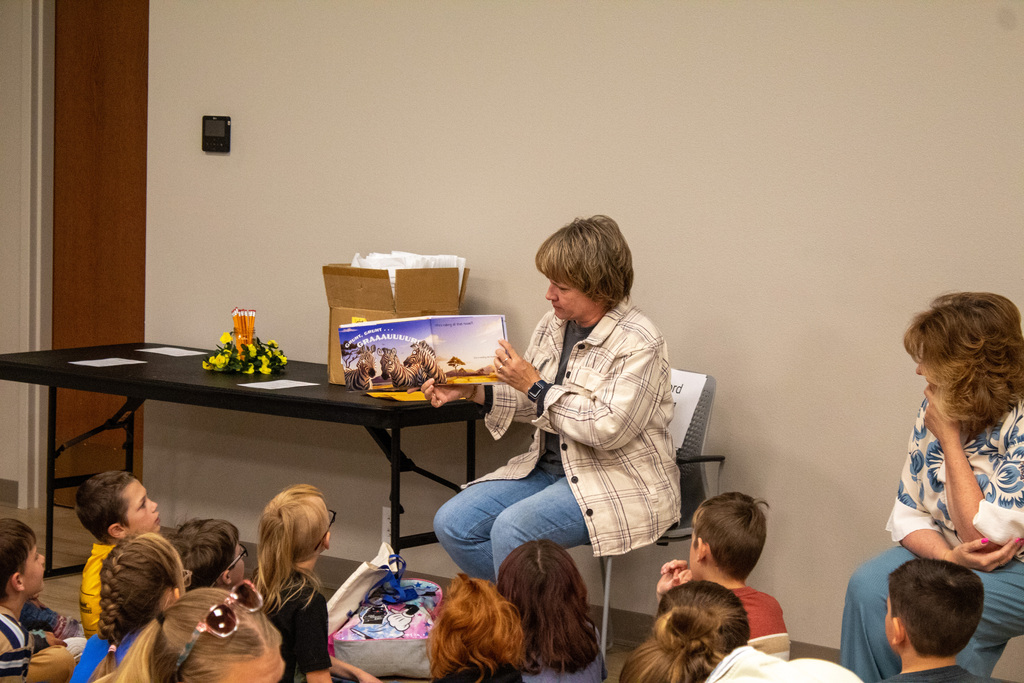 Female in jeans and a flannel reading to a group of students