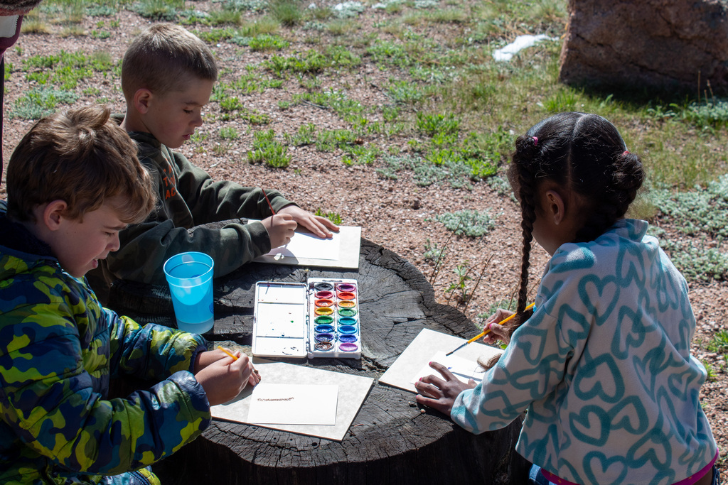 Students sitting around a stump painting with water colors
