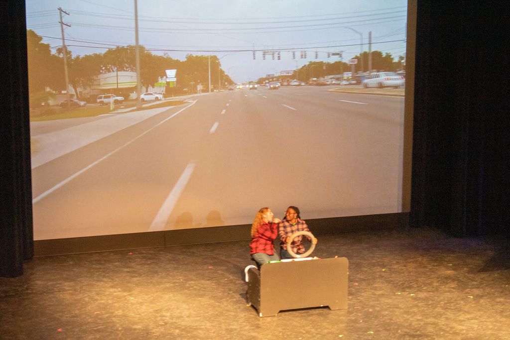 two people driving a fake cardboard car