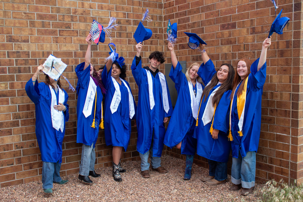 Seven students in blue garduation gowns throwing graduation caps into the air
