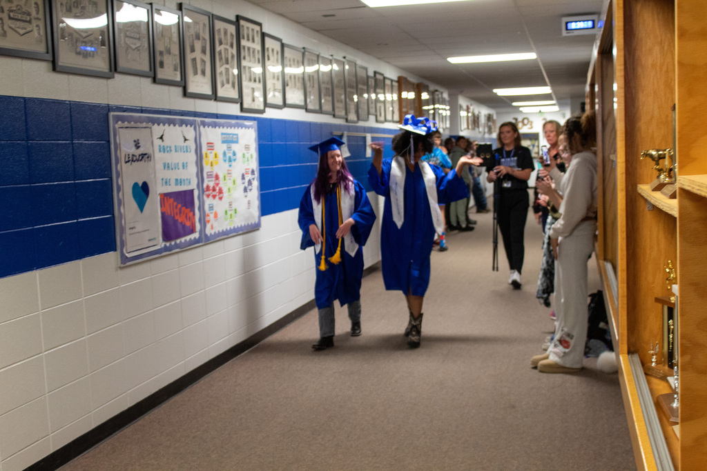 Two young woman dressed in blue caps and gowns walking down hallway