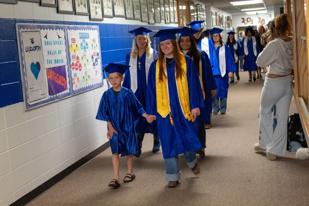 Little boy walking with older classmates in blue graduation caps and gowns