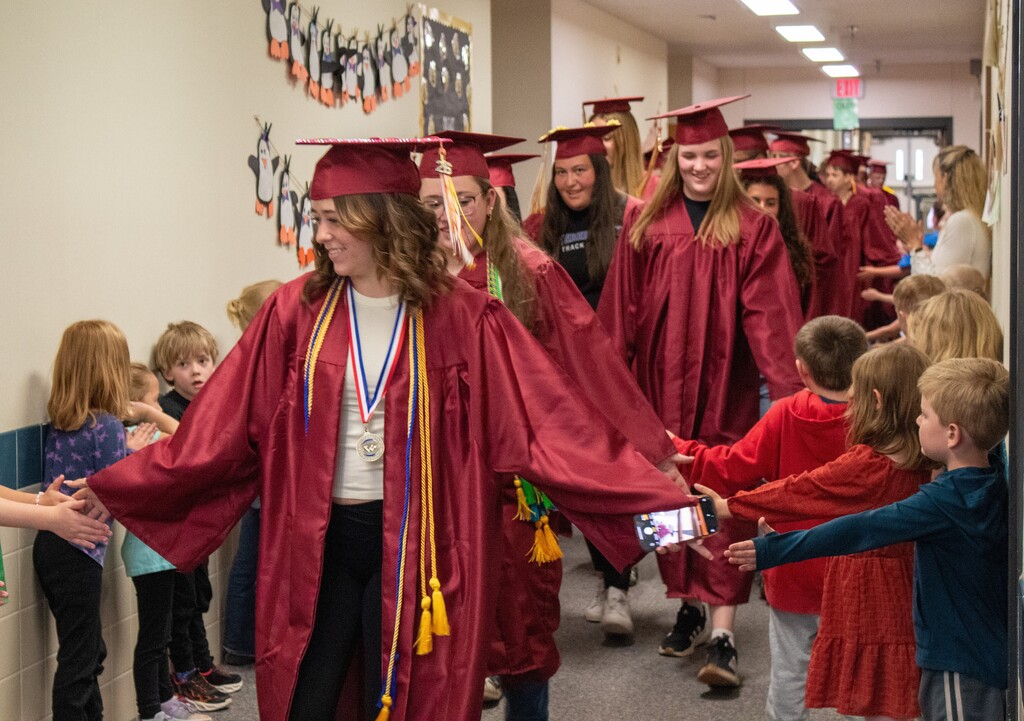 High School seniors walking down halls lined with elementary students in red caps and gowns