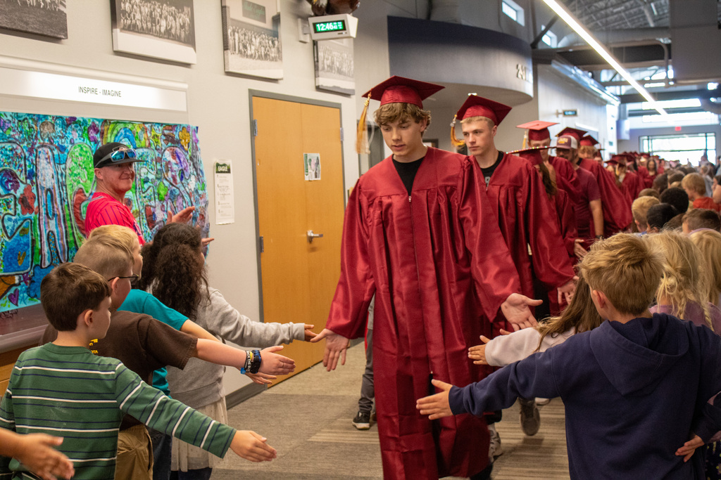 High School seniors walking down halls lined with elementary students in red caps and gowns