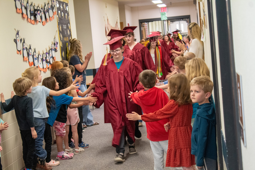 High School seniors walking down halls lined with elementary students in red caps and gowns