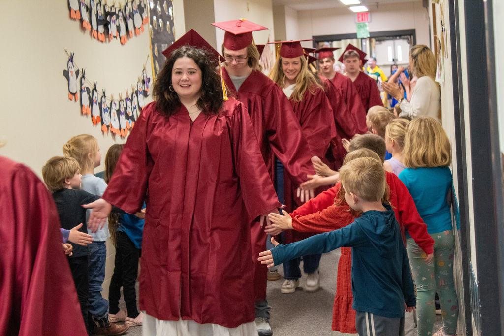 High School seniors walking down halls lined with elementary students in red caps and gowns
