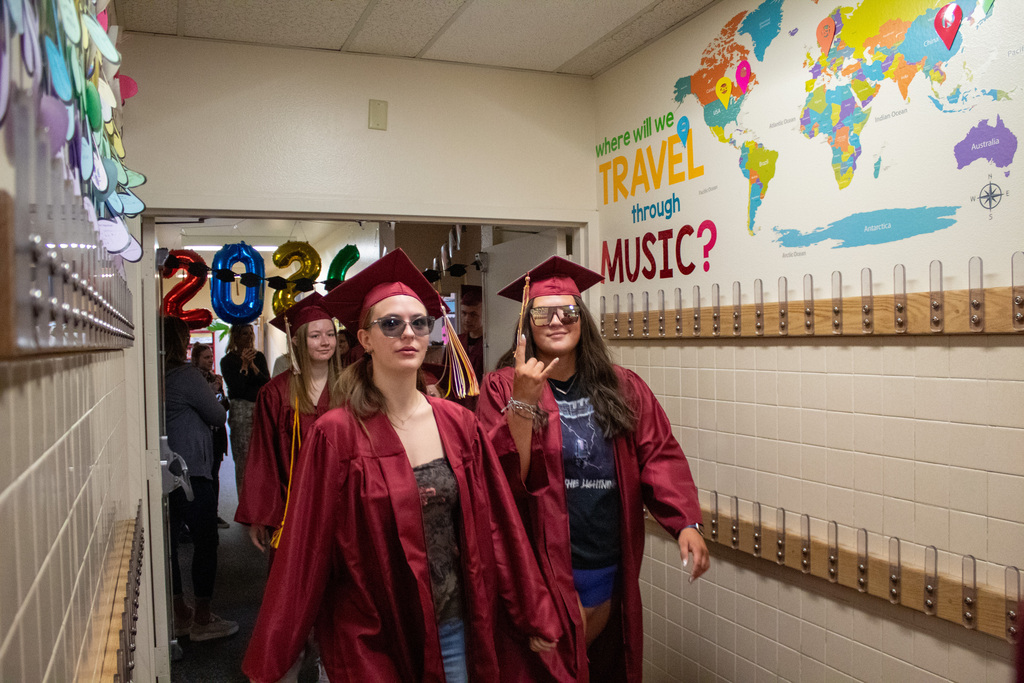 High School seniors walking down halls lined with elementary students in red caps and gowns