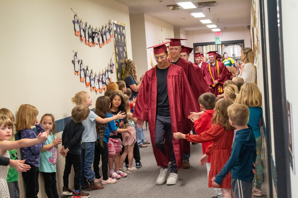 High School seniors walking down halls lined with elementary students in red caps and gowns