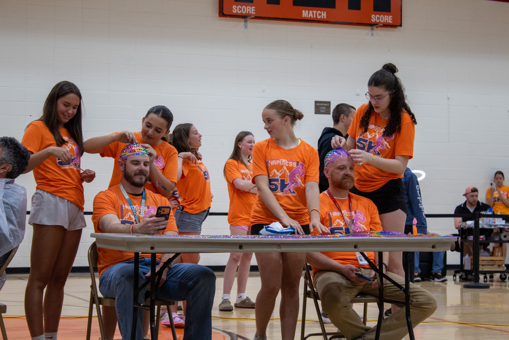 Two men getting beads glued to their head  by groups of young girls