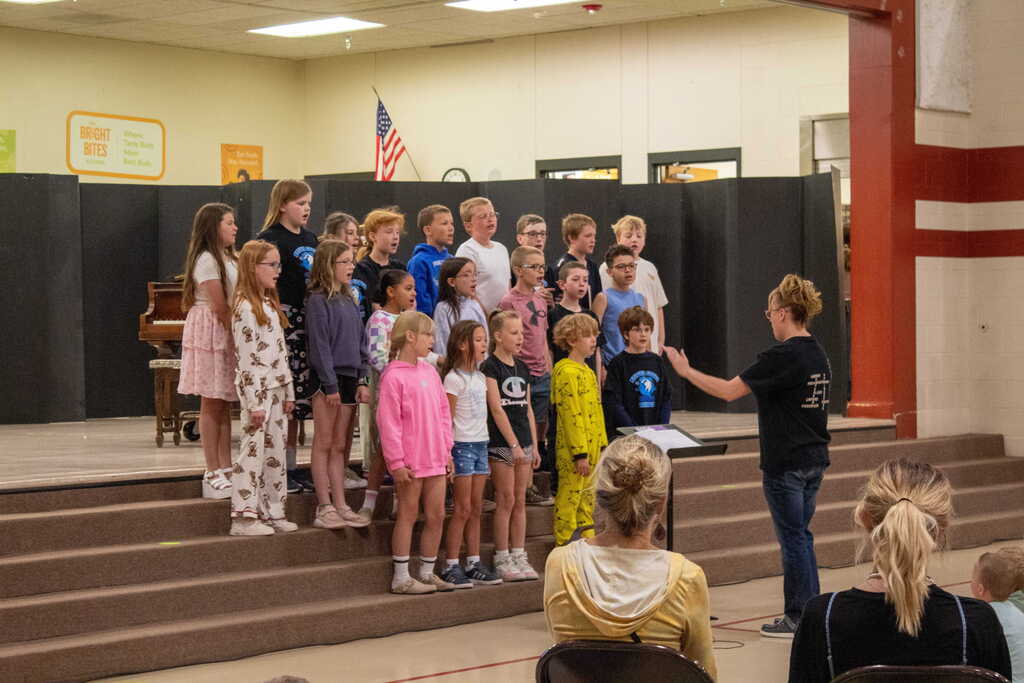 Group of students standing on a stage being directed by a teacher