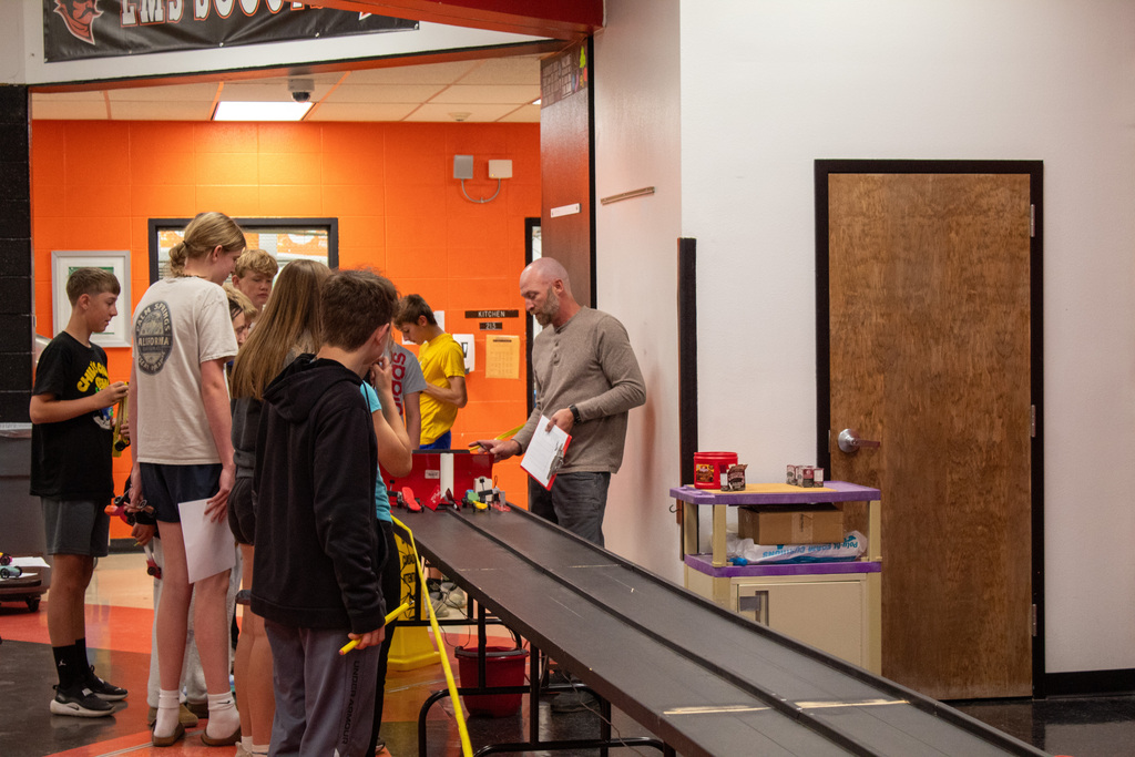 Group of students and teacher standing around a makeshift car race track