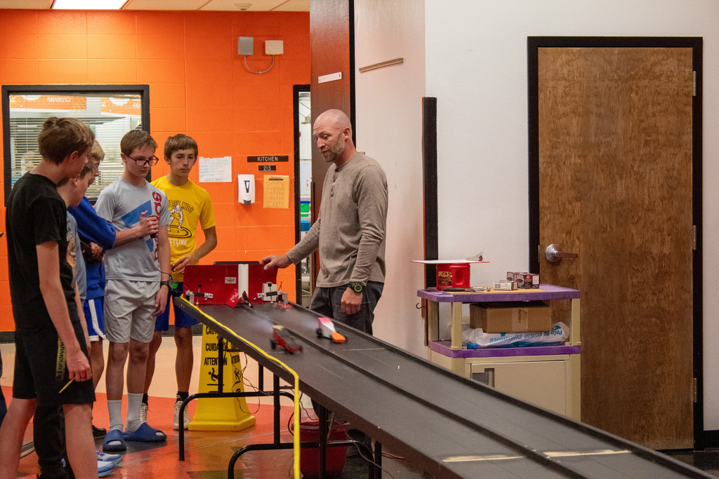 Group of students and teacher standing around a makeshift car race track