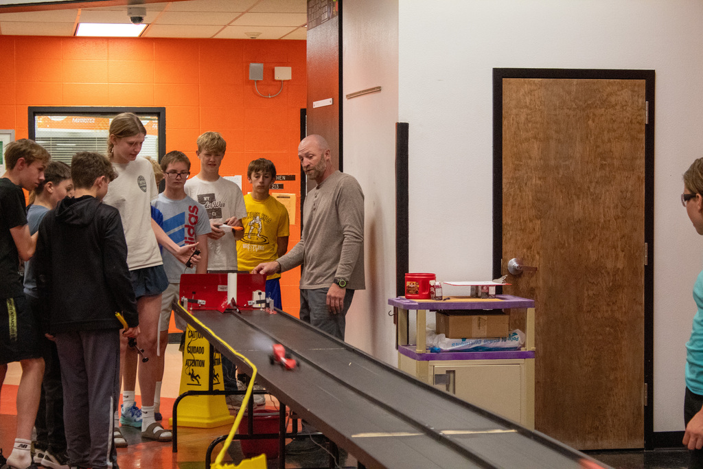 Group of students and teacher standing around a makeshift car race track
