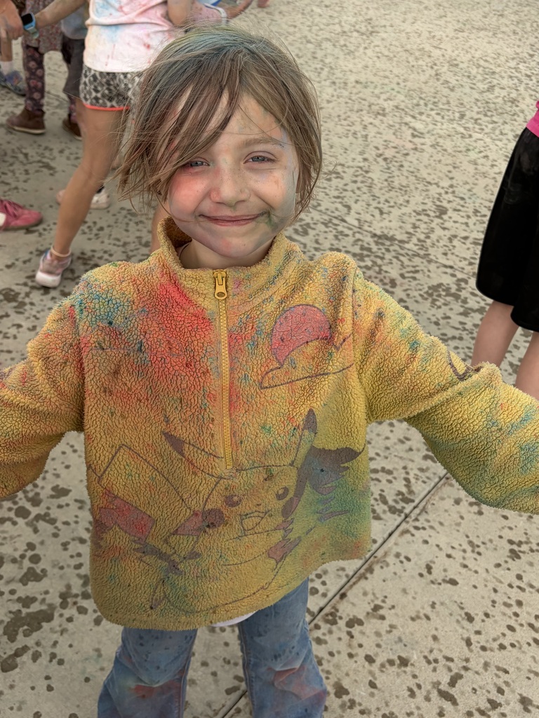 Young girl with blonde hair andyellow hoodie covered in color powder
