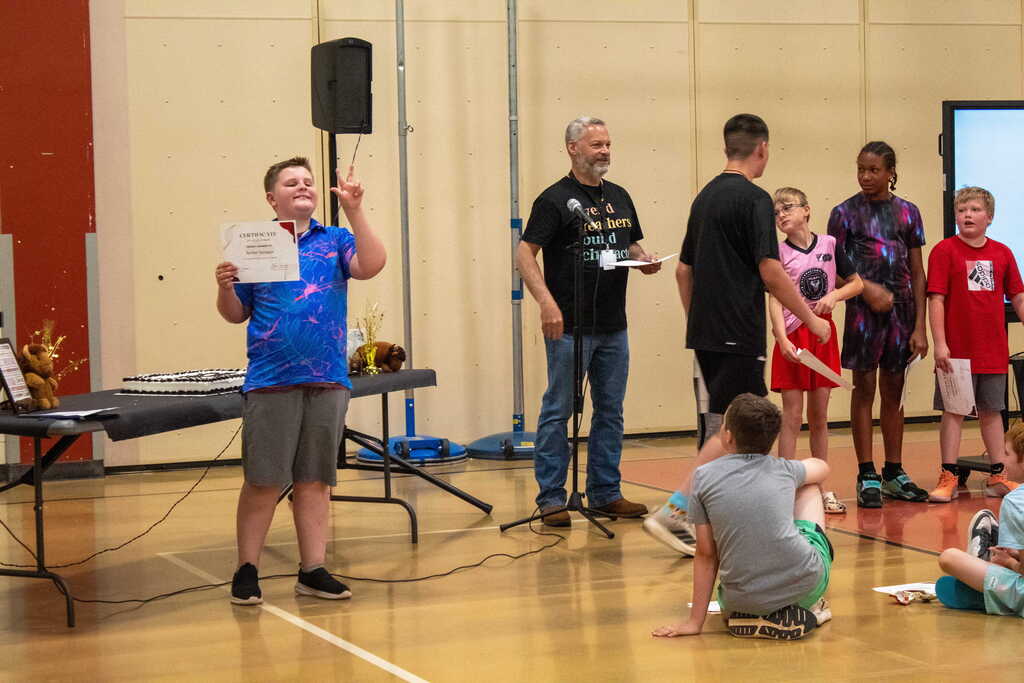 Boy in blue shirt holding a certificate waving to a crowd