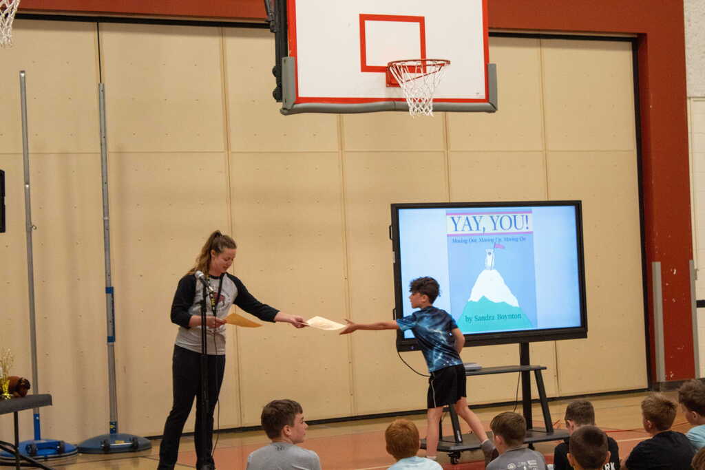 Female teacher handing young boy certificate