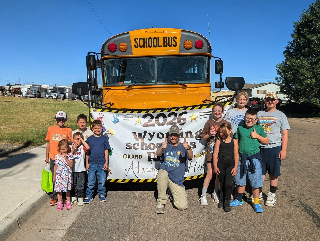 Groups of children posing with a thumbs up in front of school bus