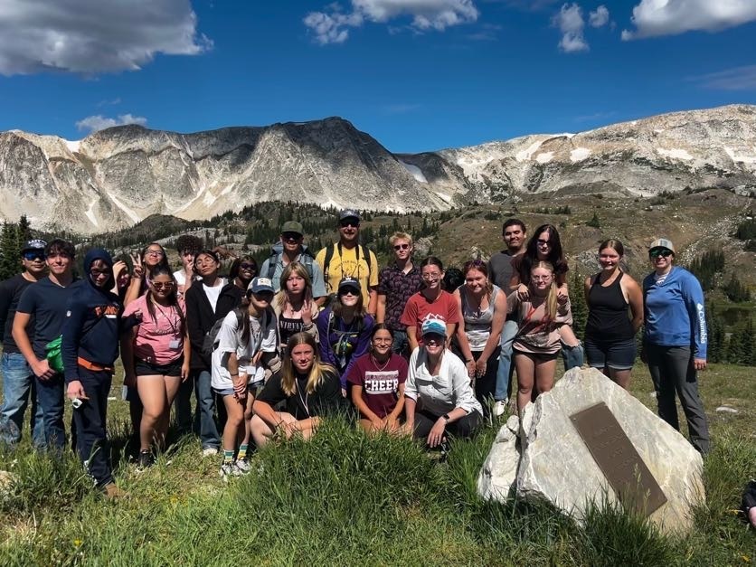 Group of students sitting in grass in front of mountain range