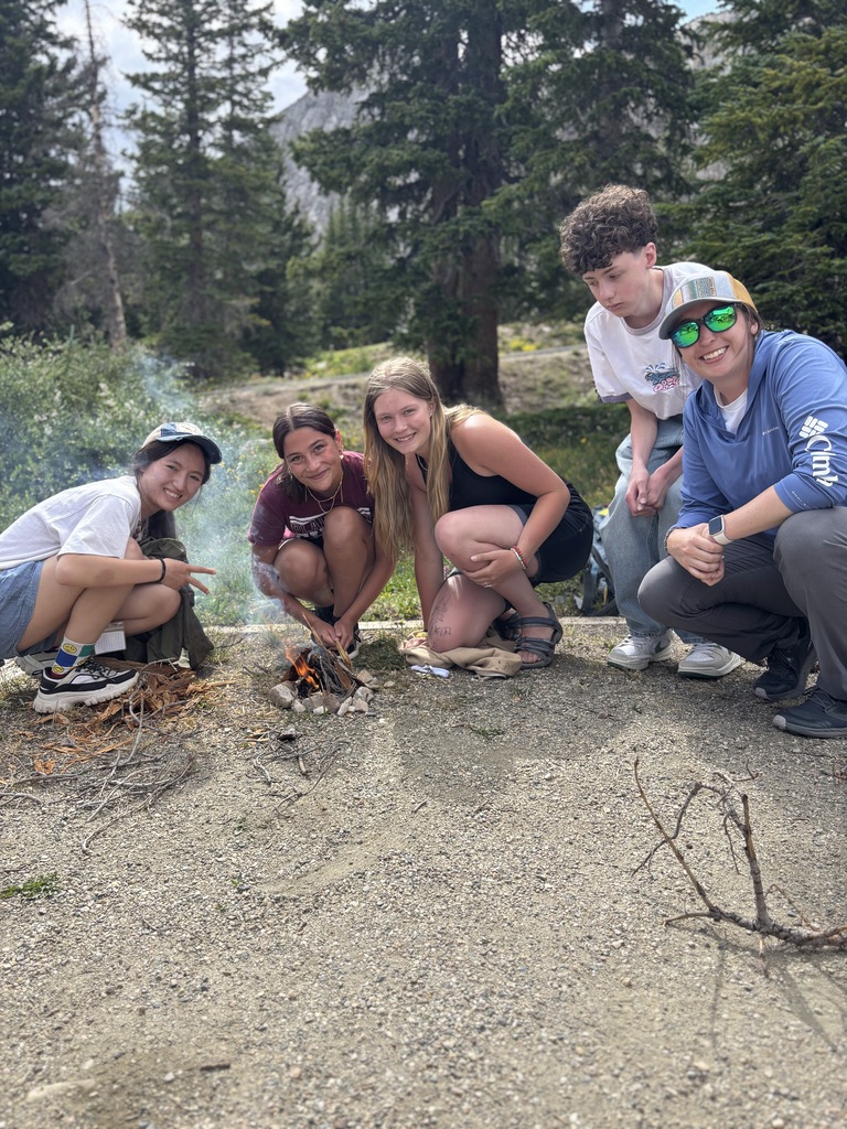Group of four students with teacher working to start a fire by hand