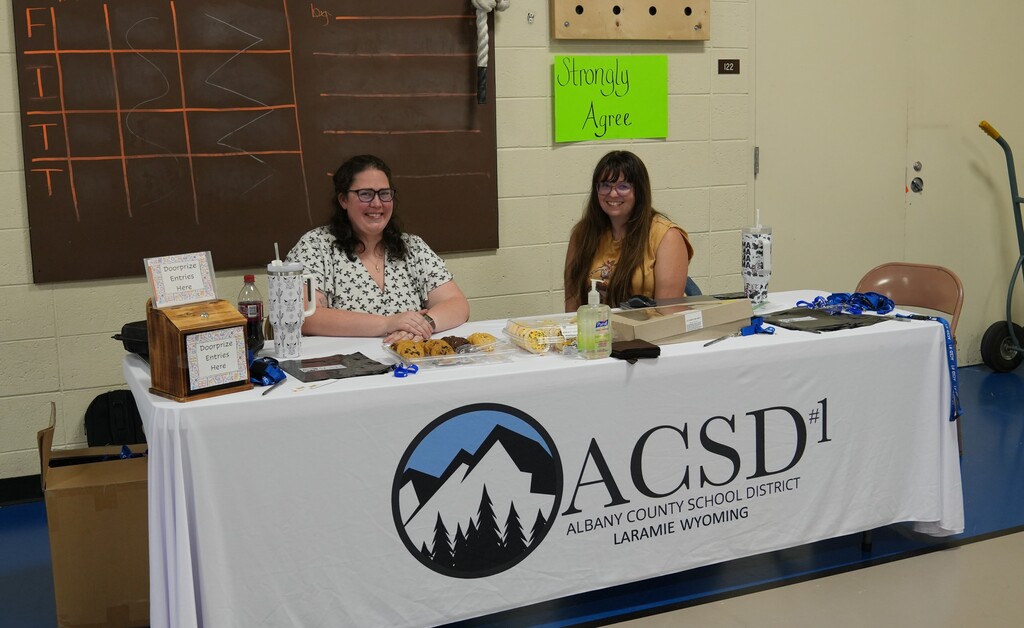 Two women sitting at a table greeting newcomers