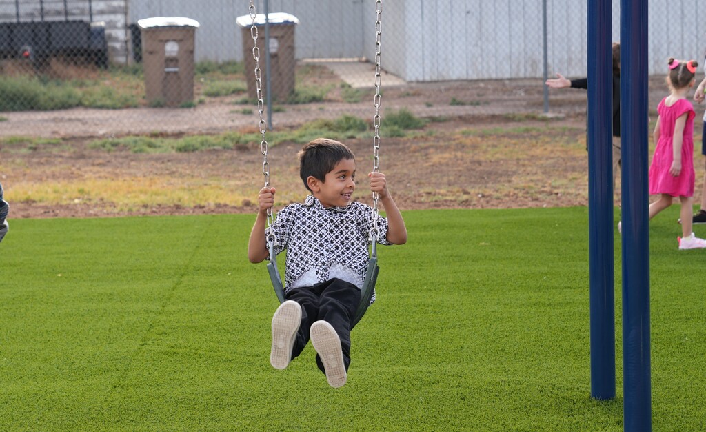 Little boy in black pants and white shirt swining on a swingset