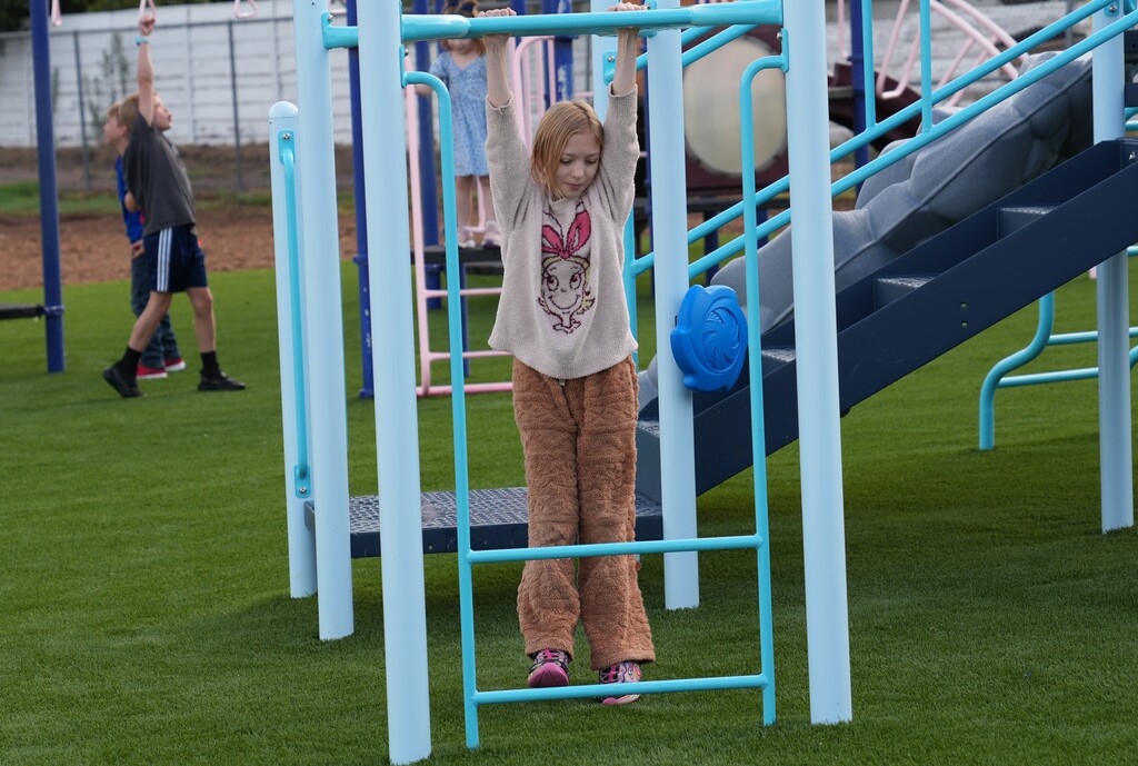 Young girl with blonde hair hanging from the monkey bars