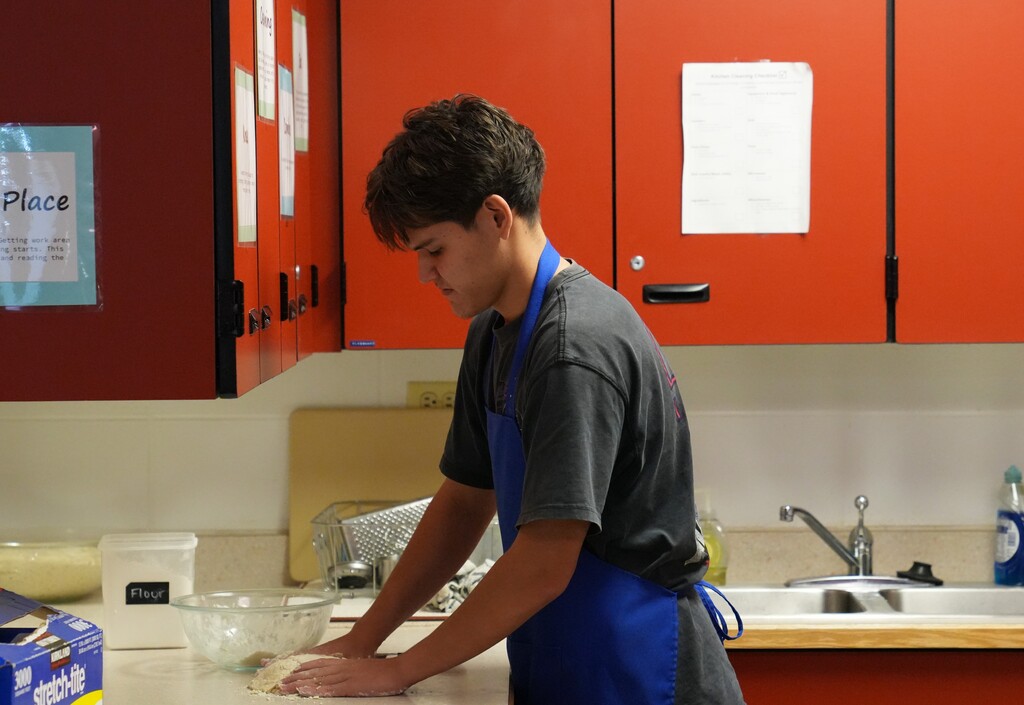 Young man with brown hair kneading dough and flour