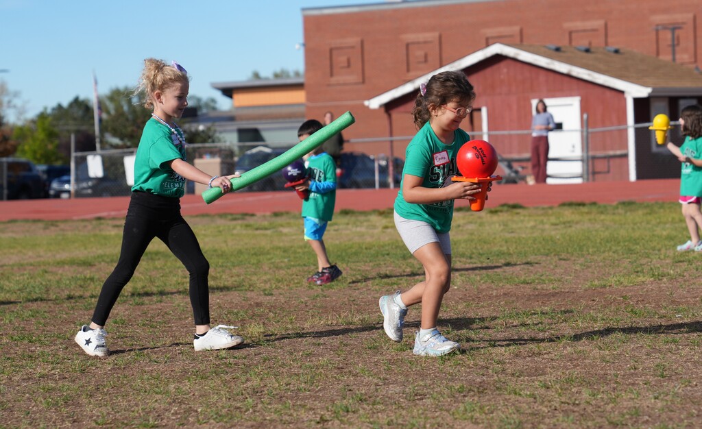 Little girl carrying a pool noodle chasing a little girl carrying a ball