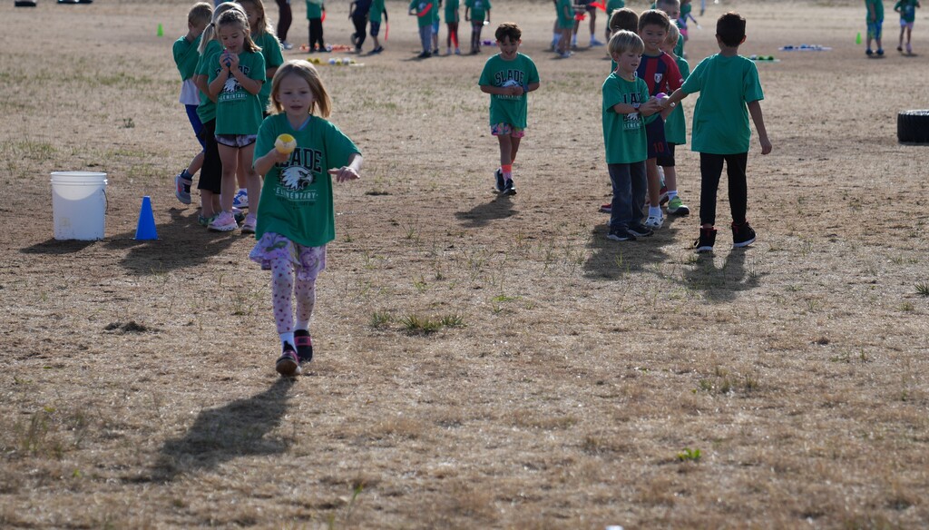 Little girl in green shirt carrying a water baloon with a spoon
