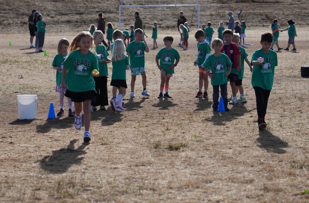 Little boy in green shirt carrying a water baloon with a spoon
