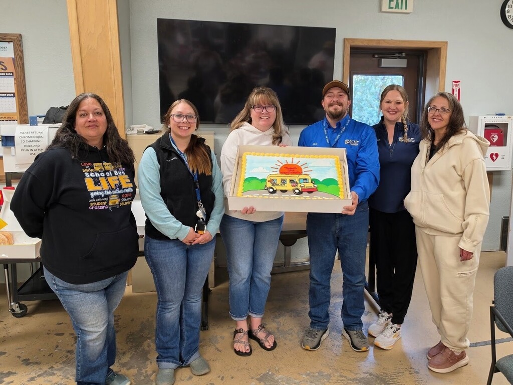 Group of men and women holding up a cake decorated with a school bus