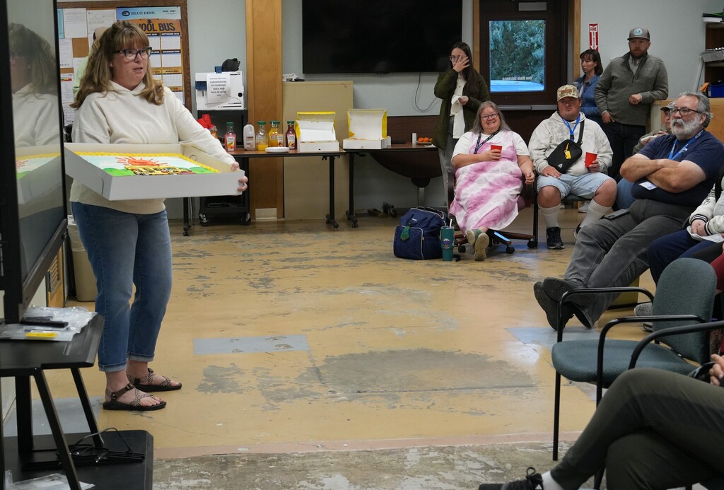 Woman presenting cake to room full of people