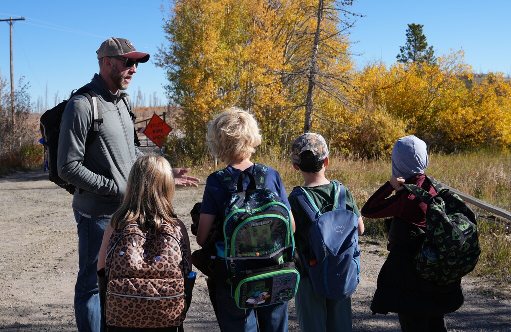 Group of boys and girls listening to teacher talk while standing outside