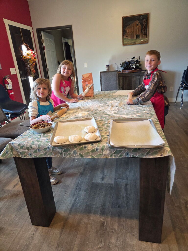 students standing around table using rolling pins to roll out dough