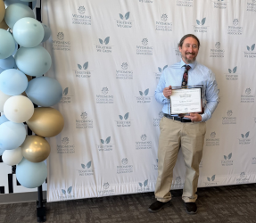 Man in tan pants with blue button down shirt holding a certificate