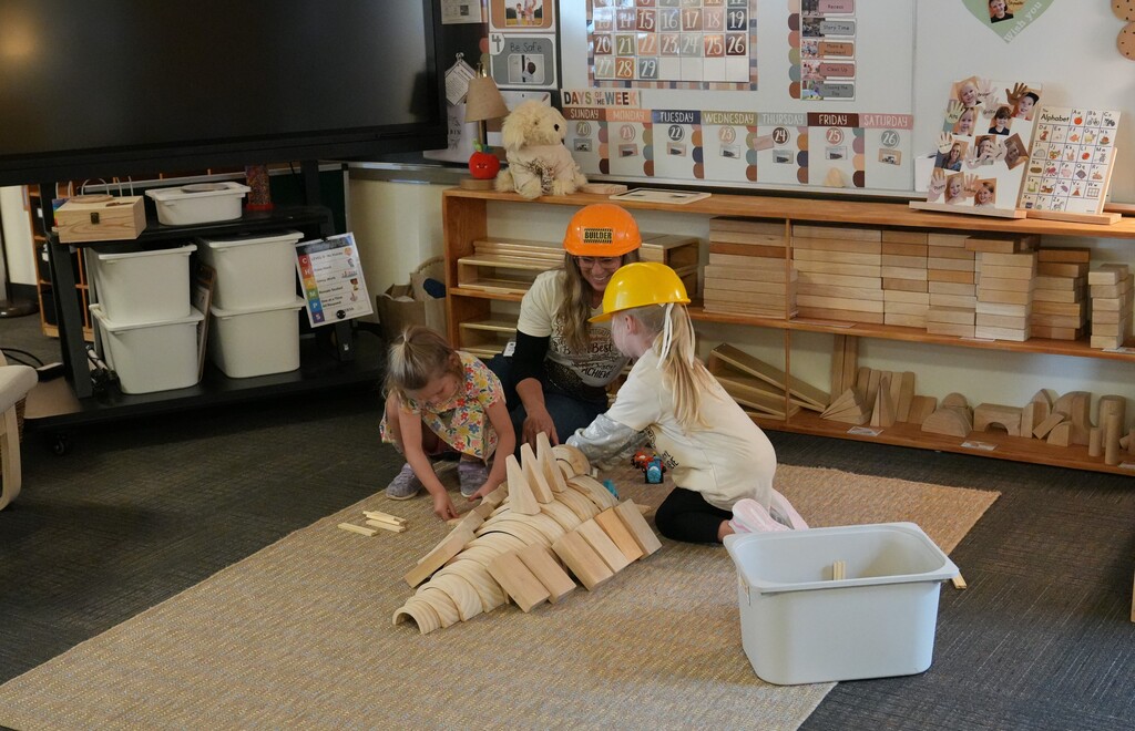 Teacher helping two young students build blocks
