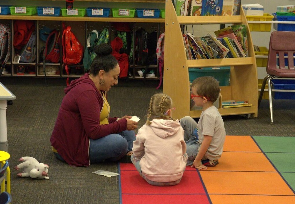 Teacher sitting on floor with two students reviewing flashcards