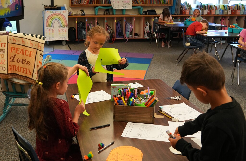 Two students cuttign green paper with scissors