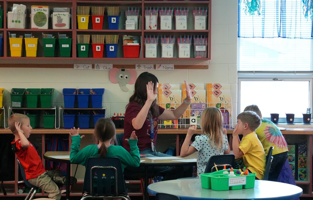 Student sitting around teacher holding up their hands