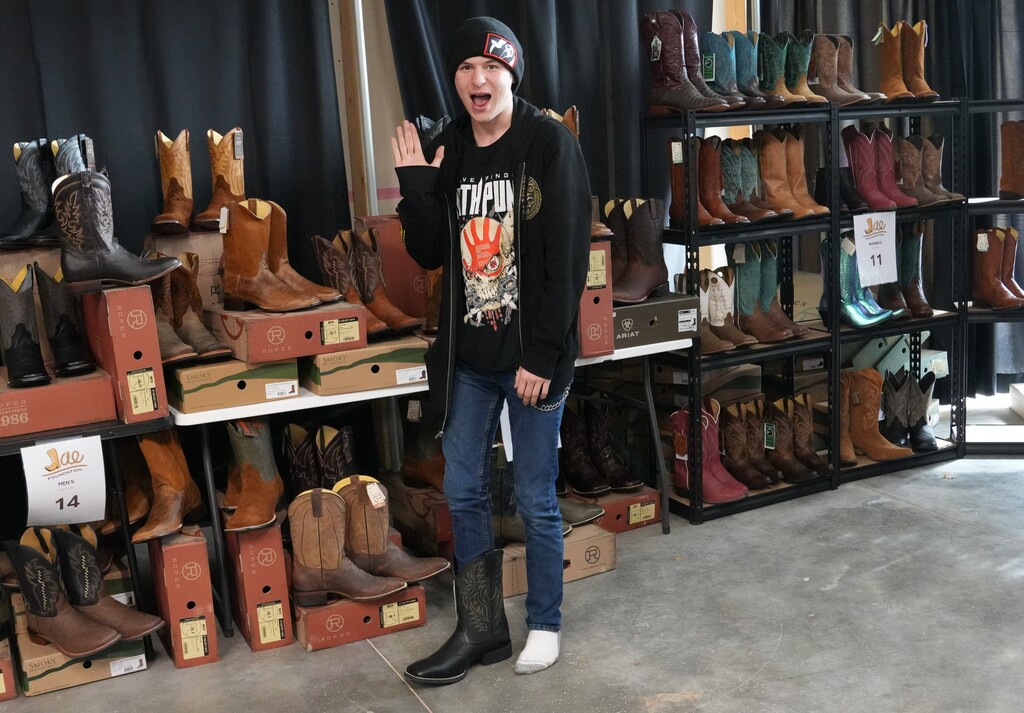 Boy in jeans and black shirt trying on black cowboy boots and waving