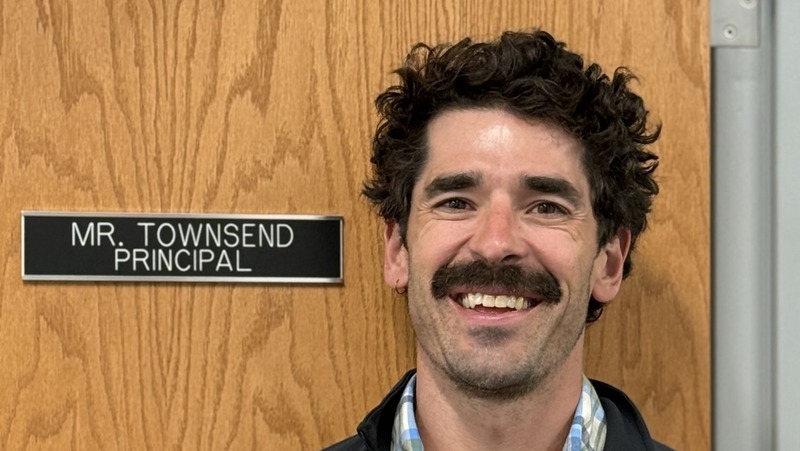 Headshot of smiling Whiting High School principal Mr. Townsend, standing in front of a wooden door with a door sign reading "MR. TOWNSEND PRINCIPA