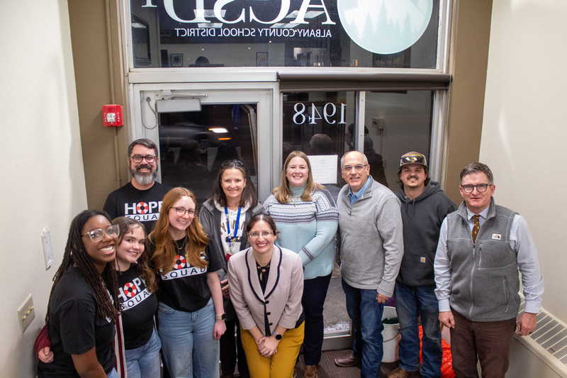 Female with brown hair presenting in front of podium as peers observe